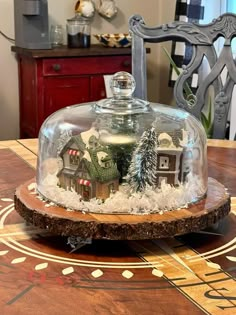 a glass clochet covered in snow with houses under it on a wooden table