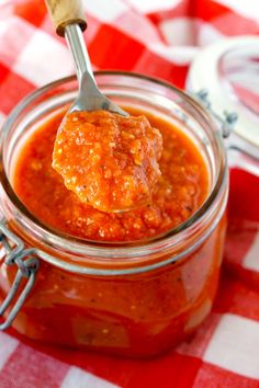 a spoon full of tomato sauce on a checkered tablecloth with a jar in the background