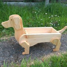 a wooden toy dachshund sitting on the ground in front of some grass