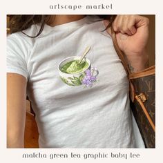 Graphic Women's Graphic Baby Tee featuring Matcha and Lavender Tea Cup. Retro Aesthetic shirt. Great gift for those who celebrate vintage charm and modern aesthetic style.  Key Features: Iconic Y2K Retro Graphic: Delight in the throwback charm with our eye-catching matcha art embodying the spirit of healthy treats in a nostalgic style. Premium Comfort: Crafted with the softest materials, this aesthetic baby tee offers both comfort and style, perfect for all-day wear. Made using ethically grown and harvested US cotton. Flattering Youth Sized Fit: Our women's baby tee is tailored to accentuate your shape while providing the comfort of a casual tiny tee. Versatile Retro Shirt: Seamlessly blends with any style, from street-smart to chic. Pair it with anything from high-waisted jeans to long sk Matcha Art, Matcha Lover, Iconic Y2k, Aesthetic Baby, Graphic Baby Tee, Lavender Tea, Baby Graphic Tees, Aesthetic Shirt, Shirt Y2k