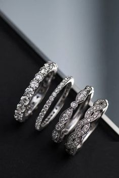 three wedding rings with diamonds on them sitting on a black surface in front of a mirror