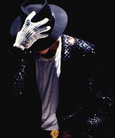 a man in a black hat and jacket with his hands on his face wearing a sequined coat