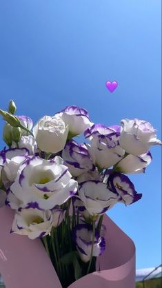 purple and white flowers are in a pink vase with hearts floating above the blue sky