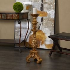 a gold candle holder sitting on top of a wooden floor next to a chair and table