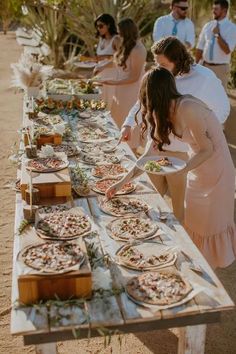 a long table with pizzas on it and people standing around the table eating them