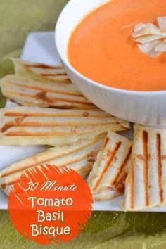 there is a bowl of tomato basil bisque on the plate with pita bread