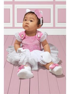 a baby sitting on the floor wearing a pink and white dress