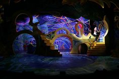 the stage is lit up with colorful lights and trees on it's sides, while a man stands in front of an elaborately designed tree - like structure