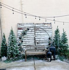 a bench sitting in front of a wooden fence with christmas trees around it and lights strung from the poles