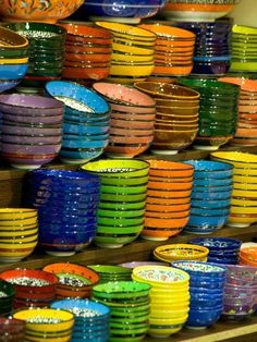 many colorful plates stacked on top of each other in front of a wooden shelf filled with bowls