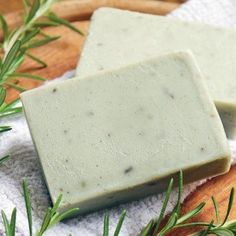 two bars of soap sitting on top of a wooden cutting board next to rosemary sprigs