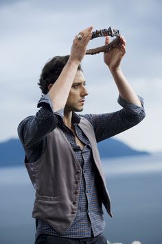 a man is holding his hat over his head while looking into the distance with mountains in the background