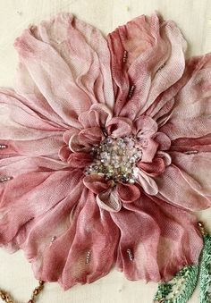 a large pink flower sitting on top of a piece of cloth next to a necklace