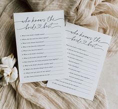 two wedding game cards sitting on top of a bed next to a white flower and cloth