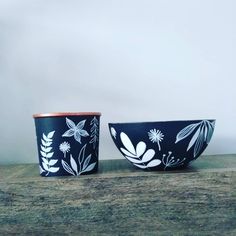 two black and white bowls sitting next to each other on a wooden table with flowers painted on them