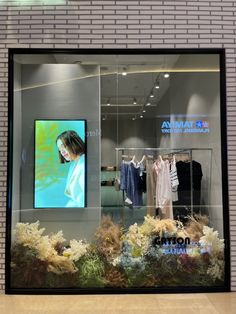 a window display with clothes and plants in it's glass front windows, displaying an image of a woman on the screen