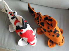 two stuffed koi fish are sitting on a couch with one laying next to the other