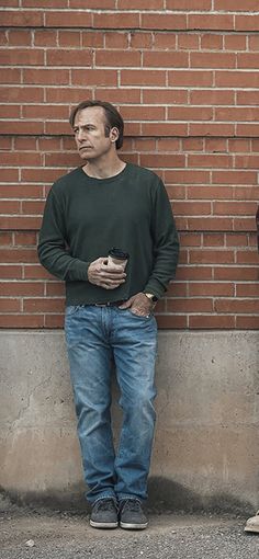 two men standing next to each other in front of a brick wall with one holding a cell phone