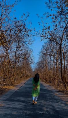 a woman walking down the middle of a road with trees lining both sides and blue sky in the background