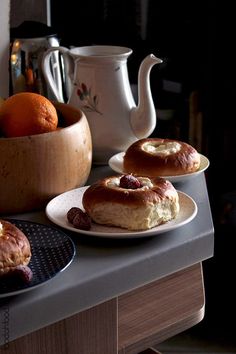 two plates with pastries sitting on a counter next to a tea pot and oranges