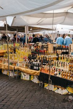 an outdoor market with lots of bottles of wine and liquor on display under white awnings