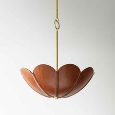 a brown leather flower hanging from a brass chain on a white wall with a light fixture in the background