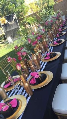 the table is set up with black and gold plates, pink napkins, and flowers