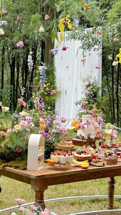 a table with flowers and desserts on it in the middle of a garden area