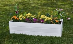 a white planter filled with lots of flowers on top of a lush green field