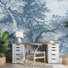 a desk with drawers and a lamp in front of a wallpapered tree mural