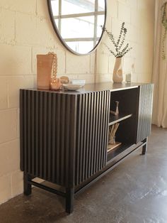 a black sideboard with a round mirror on the wall above it and a vase in front of it