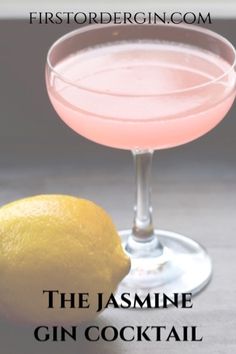 a pink drink in a glass next to a lemon