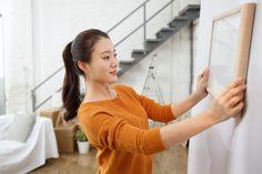 a woman is drawing on the wall in her living room with white walls and stairs