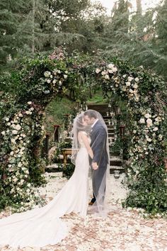 a bride and groom standing under an arch covered in flowers