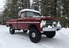 an old red truck is parked on the snow covered road in front of some trees