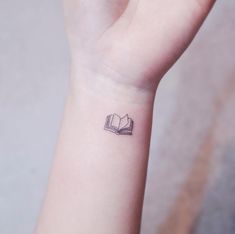 a small tattoo on the wrist of a girl reading a book with an open bookmark