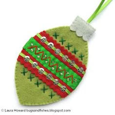 a felt ornament hanging from a green cord on a white surface with a red and green design