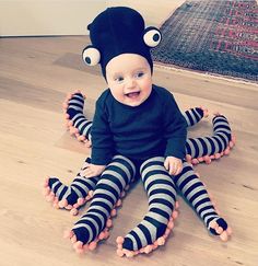 a baby sitting on the floor wearing black and white striped socks with an octopus hat