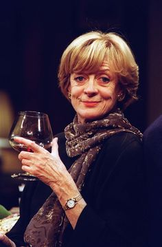 a woman holding a glass of wine in her right hand and smiling at the camera