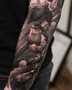 a man's arm with a bird and leaves tattoo on the left forearm, in black and white