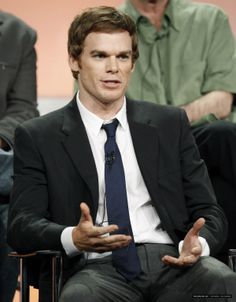 a man wearing a suit and tie sitting in a chair with his hands out to the side