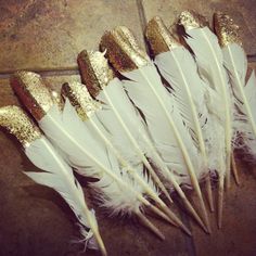 white feathers with gold glitter on them are lined up in a row against a tile floor