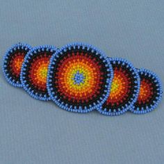 four beaded coasters are arranged on a blue tablecloth with an orange, yellow and red design