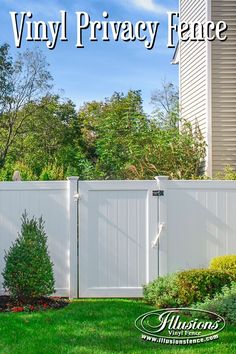 a white privacy fence in front of a house with trees on the lawn and bushes behind it