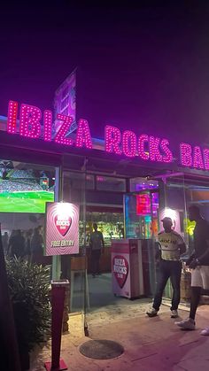 people are standing in front of a building with neon signs on the side of it