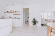 a kitchen with white walls and wooden shelves next to a dining room table in front of a couch