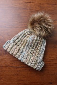 a knitted hat with a fur pom sits on top of a wooden table