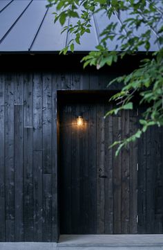 an open wooden door in front of a black building with a metal roof and light fixture