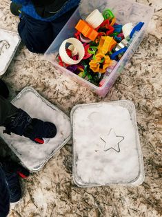 two plastic trays filled with toys on top of a marble counter next to a child's feet