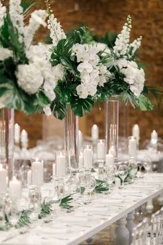 the table is set with candles and vases filled with white flowers, greenery